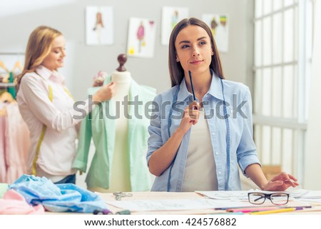 Beautiful designer is working in dressmaking studio, looking away and thinking, in the background another designer is working with jacket
