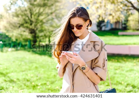 Beautiful young woman in fashionable clothes in sunglasses. Woman with long beautiful hair. She holds a mobile phone. Social networking