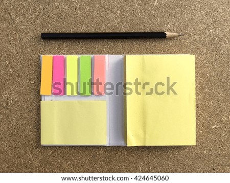Retro brown plywood with book of colorful sticky notes and pencil.