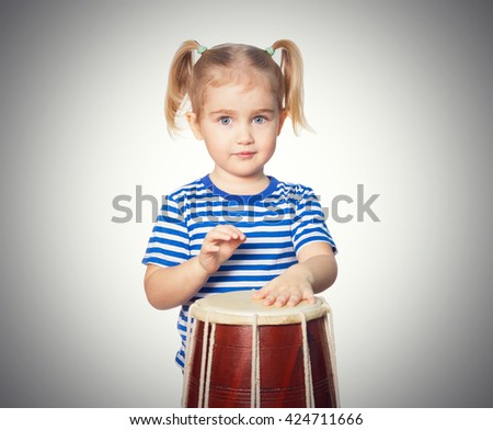 Little Funny girl in striped shirt play drum. Isolated on gray background