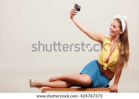 Happy smiling pretty pin up girl wearing hairband bow, skirt and high heels taking photo picture with camera. Attractive gorgeous young retro woman photographing.