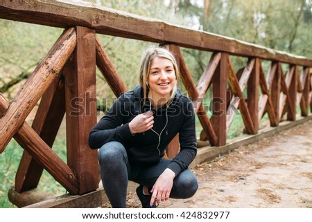 Portrait of the sports girl in fitness exercise in the woods, listening to music on headphones with the phone close emotional pictures girl in sportswear