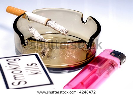 Picture of half burned cigarette in ash tray with pack of cigarettes with visible sign Smoking kills and lighter.