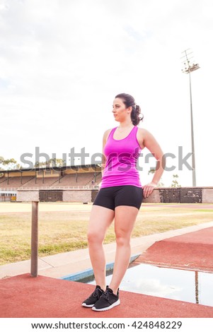 Young Brunette woman training / stretching at a track and field sports stadium with golden light.