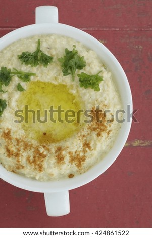 bowl of homemade chickpea hummus with olive oil, cayenne pepper and parsley. Red background