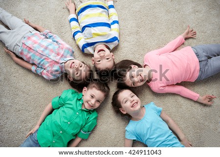 childhood, fashion, friendship and people concept - group of happy smiling little children lying on floor