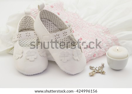 Pair of white baby shoes on embroidered christening white dress, cross and candle Royalty-Free Stock Photo #424996156
