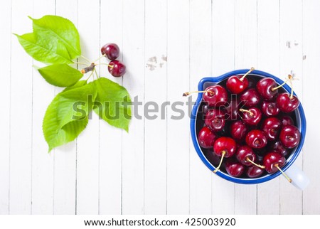 ripe cherry fruits in old style enamel iron jar, on white wooden table