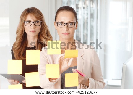 Portrait of two creative professional woman standing at office in front of idea board and thinking on new idea. 