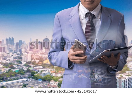 Photo of businessman holding smart phone and tablet. Double exposure photo of  city view  blur background