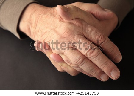 An older man grasps his hand on a black background with copy space.
