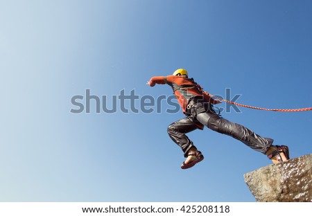 Man jumping off a cliff with a rope on a sunny day. Royalty-Free Stock Photo #425208118