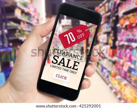 Hand holding mobile phone with sale tag and supermarket blur background.