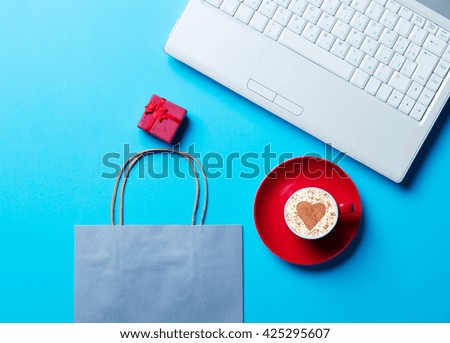cup of coffee, blue shopping bag, gift and laptop on the blue background
