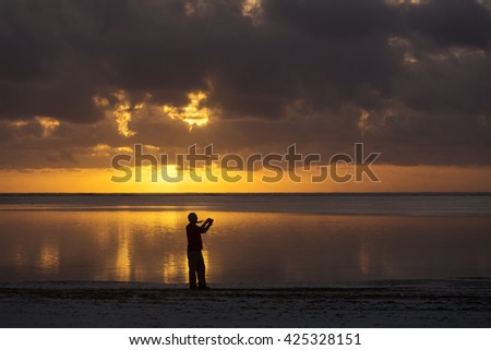 Photographer taking pictures at sunset on beach with colorful and beautiful clouds