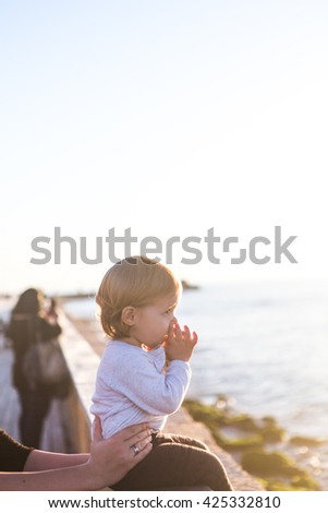 A beautiful blonde baby girl seat on the sea on a sunset. 