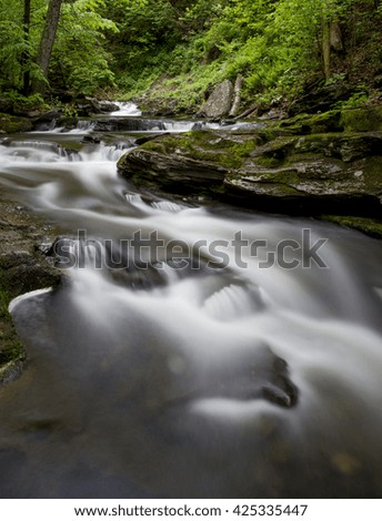 A long exposure of a scenic waterfall landscape in a bright green spring forest.