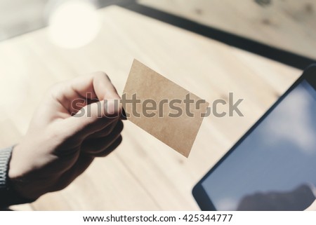 Closeup Man Showing Blank Craft Business Card, Holding Hand Modern Digital Tablet.Wood table Blurred Background.Mockup Ready  Private Information.Sunlight Reflections Screen Gadget.Horizontal mock up