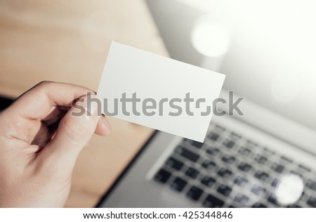 Closeup Photo Man Showing Blank Craft Business Card and Using  Modern Laptop Blurred Background. Mockup Ready for Private Information. Sunlight Reflections Screen Gadget. Horizontal mock up