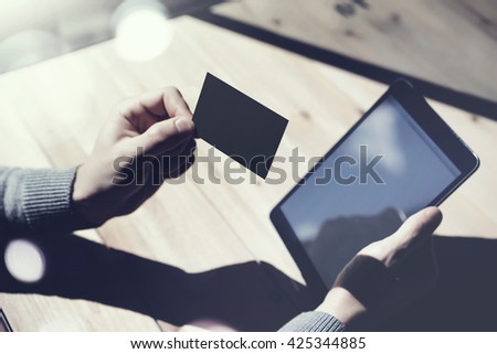Photo Man Showing Blank Black Business Card, Holding Hand Modern Digital Tablet.Wood table Blurred Background.Mockup Ready  Private Information.Sunlight Reflections Screen Gadget.Horizontal mock up