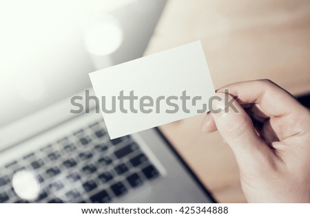 Closeup Photo Man Showing Blank White Business Card and Using  Modern Laptop on Wood table Blurred Background. Mockup Ready for Private Information. Sunlight Flares Gadget. Horizontal mock up