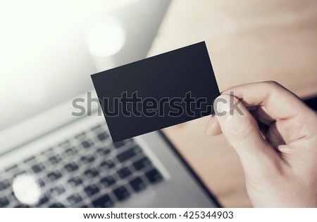 Closeup Photo Man Showing Blank Black Business Card and Using  Modern Laptop on Wood table Blurred Background. Mockup Ready for Private Information. Sunlight Flares Gadget. Horizontal mock up