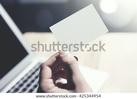 Closeup Photo Man Showing Blank White Business Card and Using  Modern Laptop Blurred Background. Mockup Ready for Private Information. Sunlight Reflections Screen Gadget. Horizontal mock up