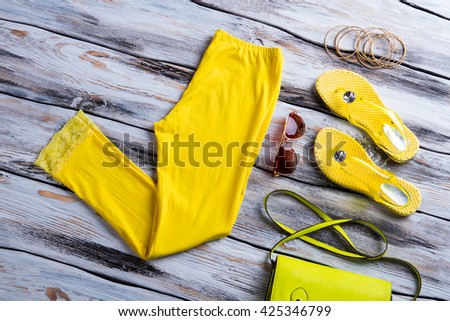 Bright yellow pants and footwear. Bracelet set with lime bag. Woman's clothing on wooden table. New items in stock.