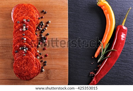 sausage or salami with chili peppers with fresh herbs colorful seasoning on black stone,wooden chopping board