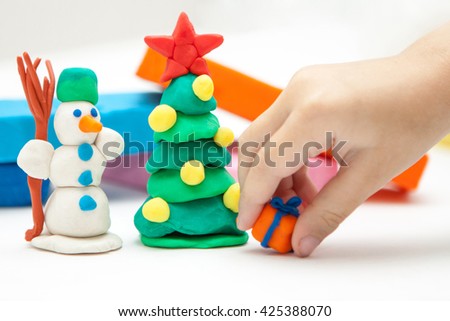 Children's craft Plasticine Christmas tree with red star and snowman. Christmas pine plasticine cartoon tree and snowman with present on a white background. A child making christmas decorations