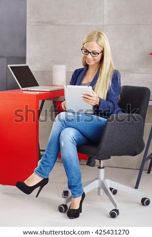 Busy blonde woman using tablet computer sitting at desk.