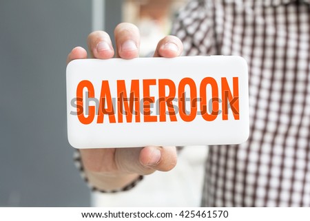 Man hand showing CAMEROON word phone with  blur business man wearing plaid shirt.