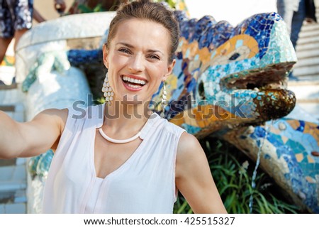 Get inspired by Park Guell in your next trip to Barcelona, Spain. Smiling young woman taking selfie near multicoloured mosaic dragon