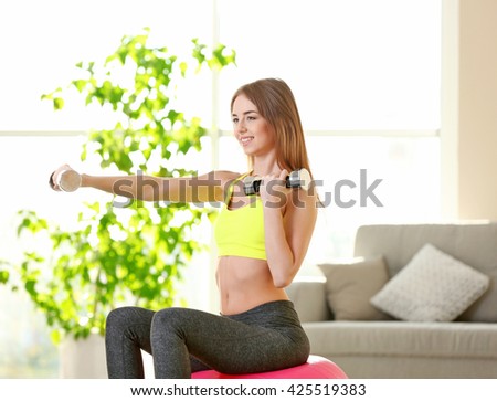Beautiful young girl doing exercises with dumbbells and fit ball at home
