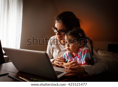 Mother and her baby girl watching cartoons on laptop.They sitting in living room.Natural light ambient.
