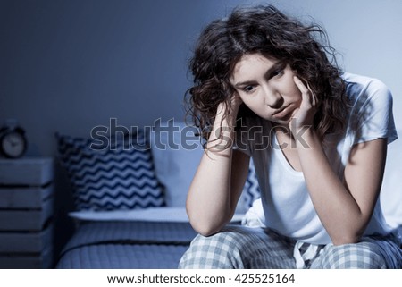 Close-up of a young woman in pyjamas sitting sleepless on the edge of her bed in the middle of the night Royalty-Free Stock Photo #425525164