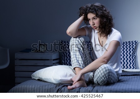 Tired and worried young woman sitting sleepless on her bed in the middle of the night Royalty-Free Stock Photo #425525467