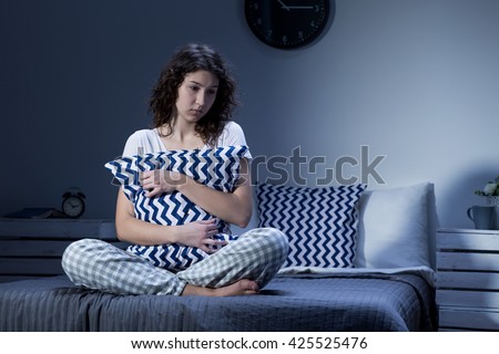 Sleepless and depressed young woman in pyjamas sitting on a bed and holding a cushion Royalty-Free Stock Photo #425525476