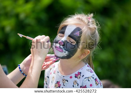 Cute little five years old girl, having her face painted as kitten on her birthday party, outdoors
