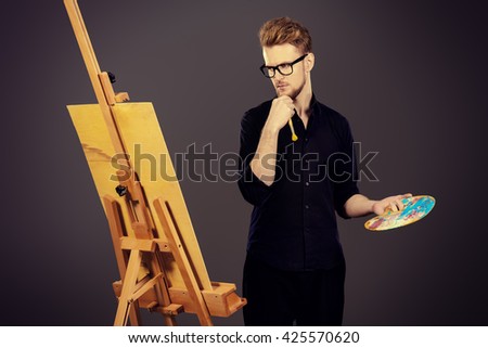 Male artist paints on an easel in the workshop. Occupation.