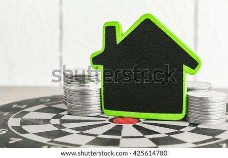 House shaped and stacked coins on dartboard over white background