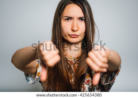Unhappy brunette girl show thumb down sign isolated on a gray background