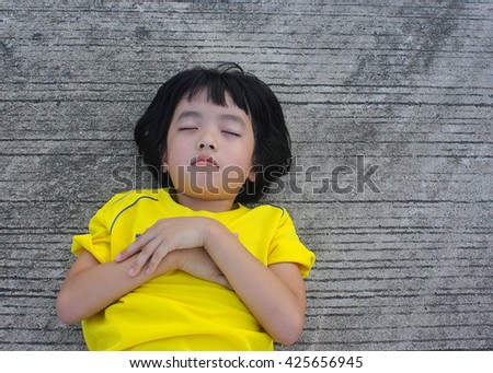 Asian little girl in a yellow T-shirt lying on the concrete floor
