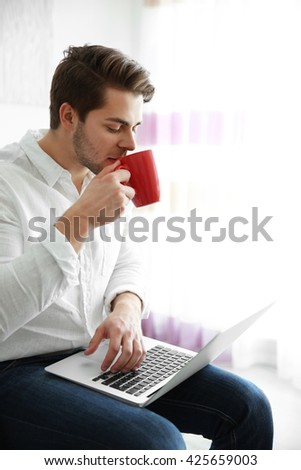 Handsome man holding laptop and drinking coffee in the morning