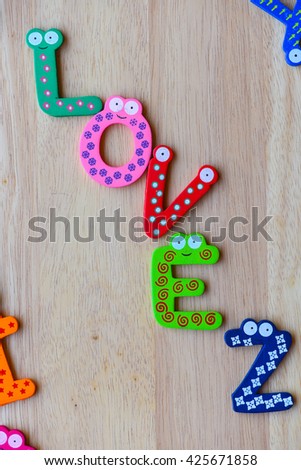 The colorful words "love" made with wooden letters next to a pile of other letters over wooden board.