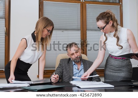 Businessman and his assistants secretaries in his office. The secretaries brought the boss documents to sign