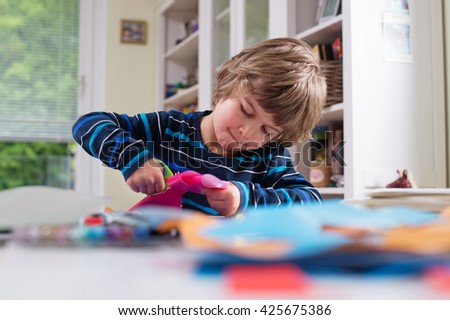 Cute little boy cutting shapes out of colored paper. Being creative, developing imagination, creativity, do it yourself concept