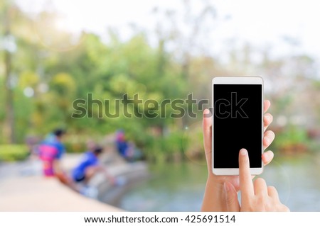 woman use mobile phone and blurred image of the park and people are feeding fishes in the pond