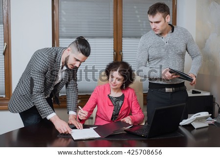 Adult woman head of business signs a contract. Businesswoman and his assistants secretaries in his office. The secretaries brought the boss documents to sign