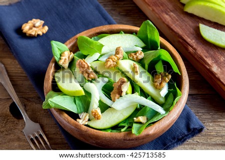 Waldorf salad with green apple, celery and walnuts in wooden bowl over rustic background